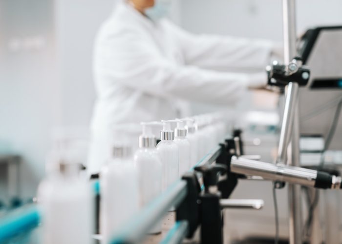 Picture of bottles with hair conditioner in row on exit of pouring machine. Chemical factory interior. In background chemist.